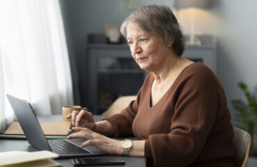 senior-woman-using-laptop-sitting-desk-living-room