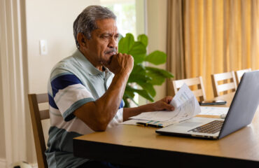 Senior biracial man doing paperwork and using laptop in dining room. Finance, retirement, domestic life, communication and senior lifestyle, unaltered.