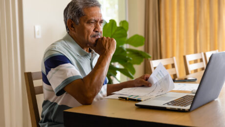 Senior biracial man doing paperwork and using laptop in dining room. Finance, retirement, domestic life, communication and senior lifestyle, unaltered.