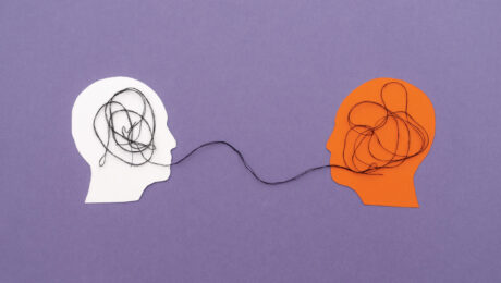 Two Paper Silhouette Heads Connected by Black Thread Symbolizing Mental Connection on Purple Background