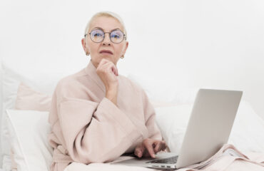 pensive-elderly-woman-posing-bed-with-laptop