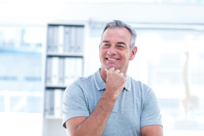 Homem de meia-idade sorrindo em ambiente de escritório, representando a possibilidade de aposentadoria aos 50 anos.