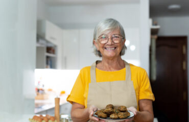 Dona de casa pode se aposentar pelo INSS. Idosa sorridente de avental segurando prato de alimentos, representando a dona de casa e seu direito à aposentadoria pelo INSS.