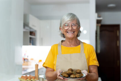 Idosa sorridente de avental segurando prato de alimentos, representando a dona de casa e seu direito à aposentadoria pelo INSS.