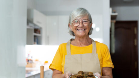 Dona de casa pode se aposentar pelo INSS. Idosa sorridente de avental segurando prato de alimentos, representando a dona de casa e seu direito à aposentadoria pelo INSS.
