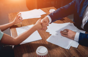 acordo-recuperacao-credito-extrajudicial Duas pessoas apertando as mãos sobre uma mesa com documentos e caneta, simbolizando acordo extrajudicial firmado entre empresa e cliente.