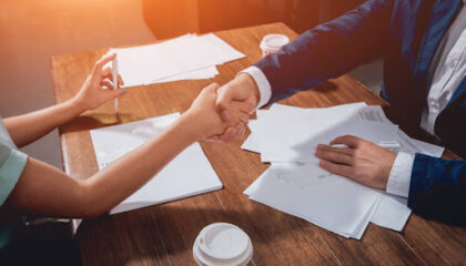 Duas pessoas apertando as mãos sobre uma mesa com documentos e caneta, simbolizando acordo extrajudicial firmado entre empresa e cliente.