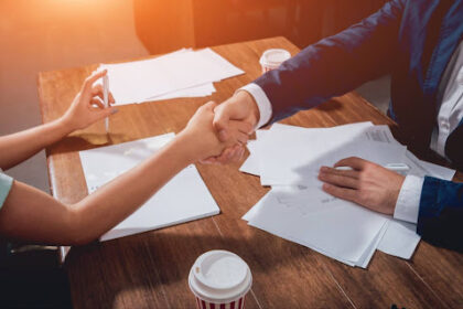 Duas pessoas apertando as mãos sobre uma mesa com documentos e caneta, simbolizando acordo extrajudicial firmado entre empresa e cliente.