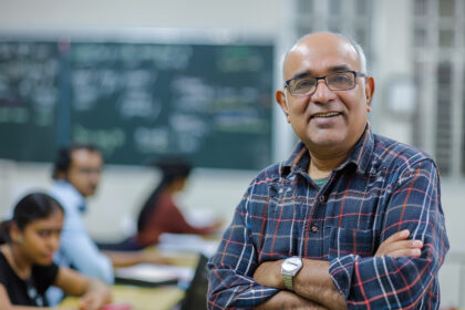 Professor com óculos e camisa xadrez sorrindo em sala de aula, representando os direitos
