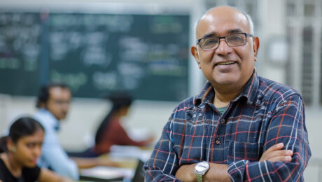aposentadoria-professor-direitos-previdenciarios Professor com óculos e camisa xadrez sorrindo em sala de aula, representando os direitos