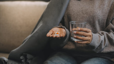 O que fazer quando o auxílio-doença é negado pelo INSS: entenda seus direitos e como agir Mulher sentada com cobertor no colo, segurando comprimidos e copo d’água, representando o momento de fragilidade durante afastamento por doença