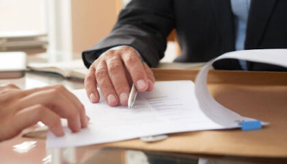 Pessoa apontando cláusula contratual em documento jurídico sobre a mesa