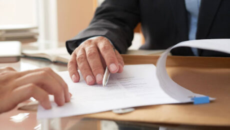 Revisão de cláusulas contratuais para proteção jurídica Pessoa apontando cláusula contratual em documento jurídico sobre a mesa