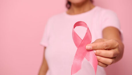 Outubro Rosa: conheça os direitos previdenciários de pacientes com câncer de mama Mulher com camiseta rosa segurando laço símbolo da campanha Outubro Rosa, representando a conscientização sobre o câncer de mama