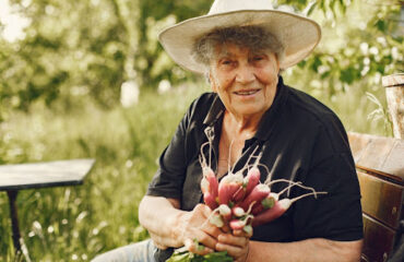 aposentadoria-hibrida-trabalho-rural-urbano Trabalhadora rural idosa sorrindo e segurando vegetais colhidos, representando o direito à aposentadoria híbrida.