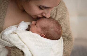 salário-maternidade Mãe segura o bebê nos braços e beija sua testa, simbolizando o cuidado e a proteção garantidos pelo salário-maternidade.