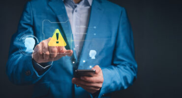 Profissional aponta para um ícone de alerta digital enquanto segura um celular, representando atenção a riscos e falhas na recuperação de crédito empresarial.