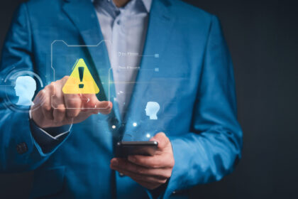 Profissional aponta para um ícone de alerta digital enquanto segura um celular, representando atenção a riscos e falhas na recuperação de crédito empresarial.