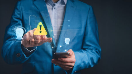 Sinais de alerta na recuperação de crédito empresarial Profissional aponta para um ícone de alerta digital enquanto segura um celular, representando atenção a riscos e falhas na recuperação de crédito empresarial.