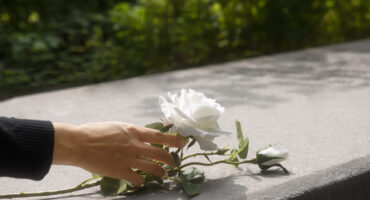 Mão colocando uma flor branca sobre um túmulo, simbolizando luto e pensão por morte no INSS.