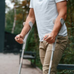 Homem utilizando muletas após lesão, representando situações que podem gerar auxílio-doença ou auxílio-acidente no INSS.