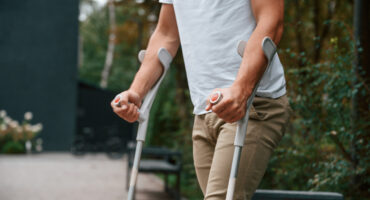 Homem utilizando muletas após lesão, representando situações que podem gerar auxílio-doença ou auxílio-acidente no INSS.