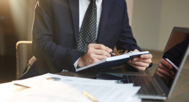 Advogado de terno analisando documentos e fazendo anotações em um escritório, representando a preparação de recurso no INSS.