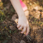 Mão de criança utilizando ferramenta de jardinagem na terra, simbolizando a possibilidade de averbar trabalho rural na infância para aposentadoria.