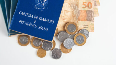 Carteira de Trabalho e Previdência Social ao lado de dinheiro em reais, representando contribuições e benefícios do INSS.