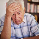 Senhor preocupado com a mão na testa após receber um indeferimento de aposentadoria do INSS.