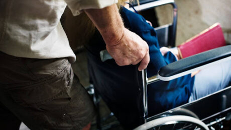 Homem idoso auxiliando mulher em cadeira de rodas, representando a necessidade de amparo e quando a doença grave dá o direito à aposentadoria por invalidez.
