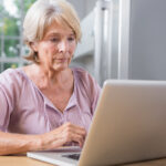 Idosa consultando informações da tabela do INSS 2026 no notebook em casa