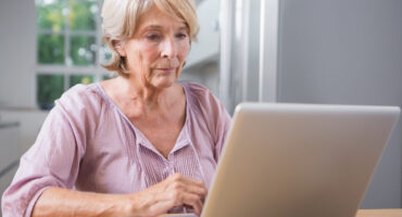 Idosa consultando informações da tabela do INSS 2026 no notebook em casa