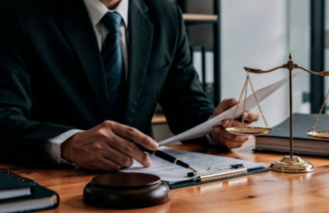 Advogado em traje formal analisando documentos sobre mesa de madeira, com balança da justiça e martelo ao lado, representando a auditoria de passivo trabalhista na sucessão de empresas.