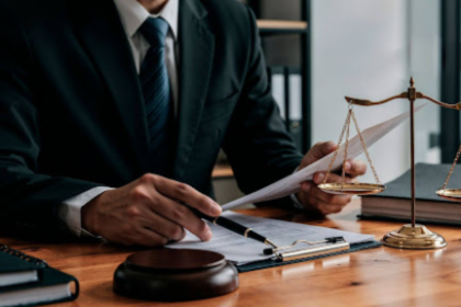 Advogado em traje formal analisando documentos sobre mesa de madeira, com balança da justiça e martelo ao lado, representando a auditoria de passivo trabalhista na sucessão de empresas.