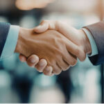 Aperto de mãos entre dois profissionais em traje formal, simbolizando a formalização de um tipo societário e o fechamento de um acordo empresarial.