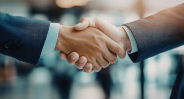 Aperto de mãos entre dois profissionais em traje formal, simbolizando a formalização de um tipo societário e o fechamento de um acordo empresarial.